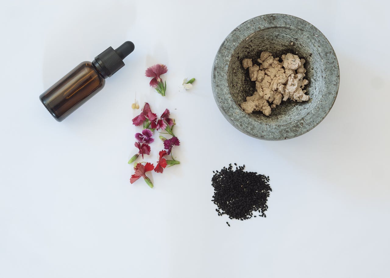 about-us Flat lay of natural skincare ingredients including flowers, black seeds, and a dropper bottle.