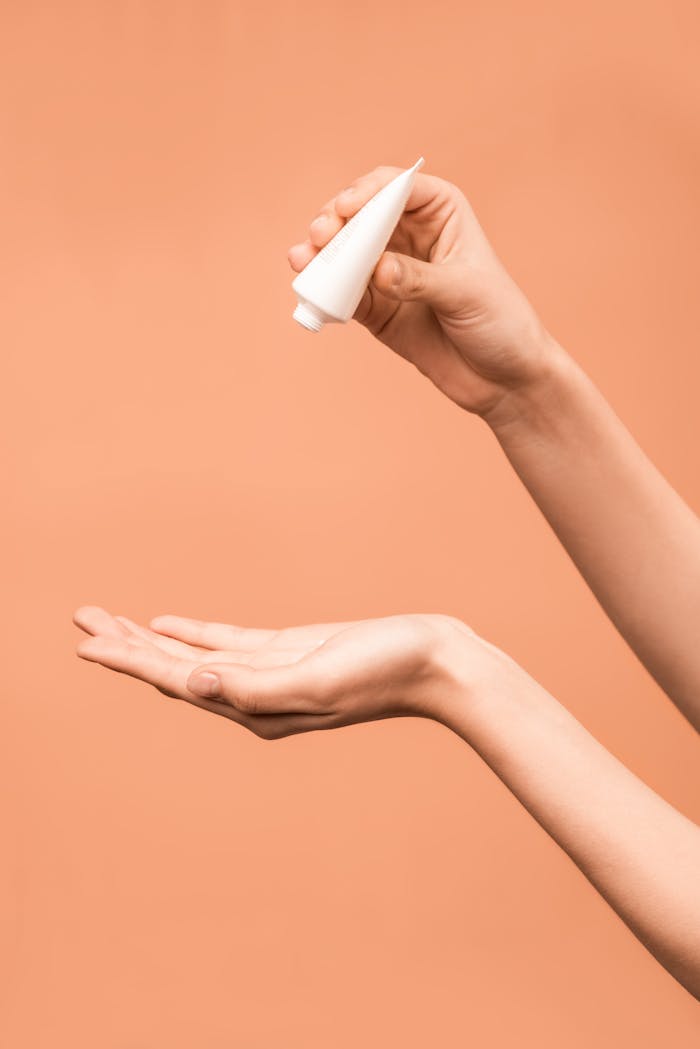 Close-up of hands applying lotion from a tube against a peach background.
